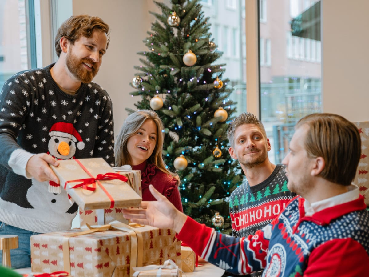 Kollegor som delar ut julklappar framför granen – skattefria gåvor till anställda
